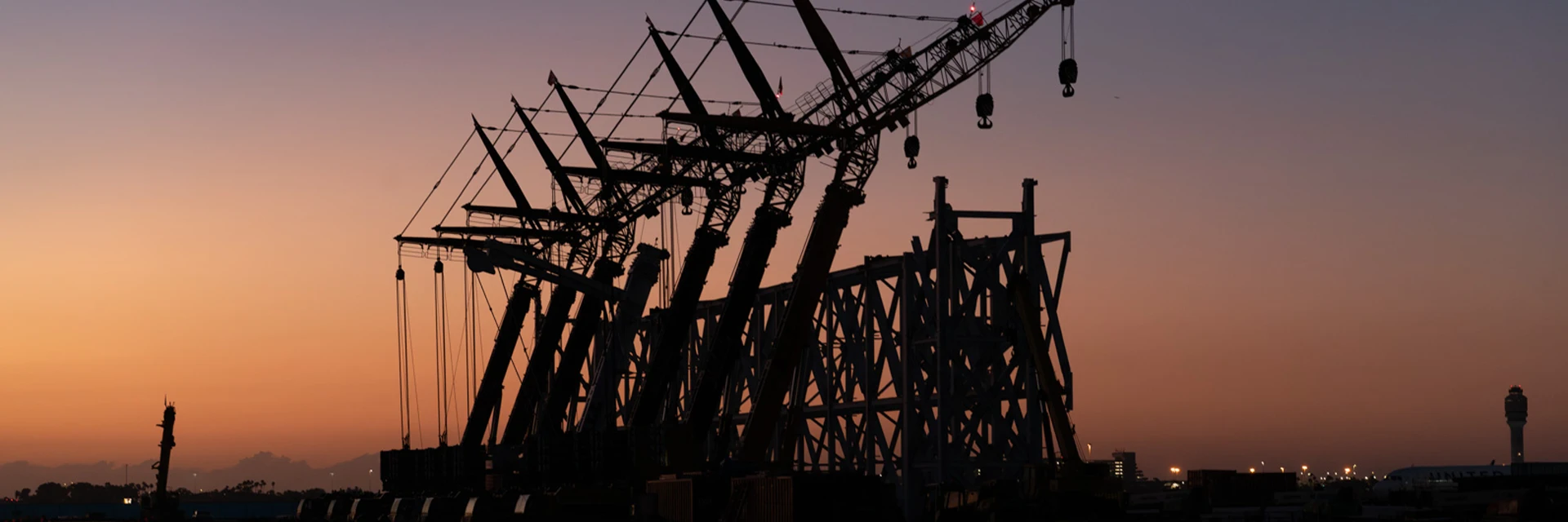 Seven all-terrain cranes lifting airport hangar truss at sunset