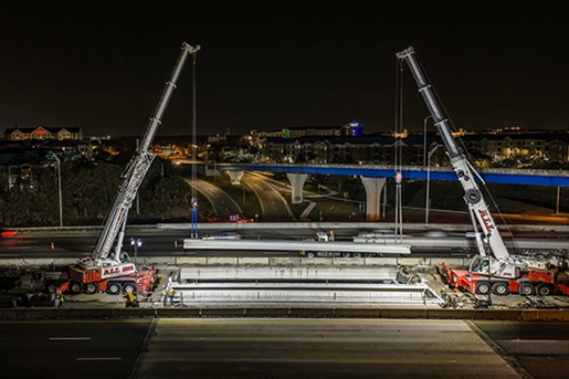 Two Liebherr AT's dual picking a bridge beam at night