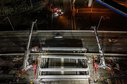Aerial view of two Liebherr AT's dual picking a bridge beam at night