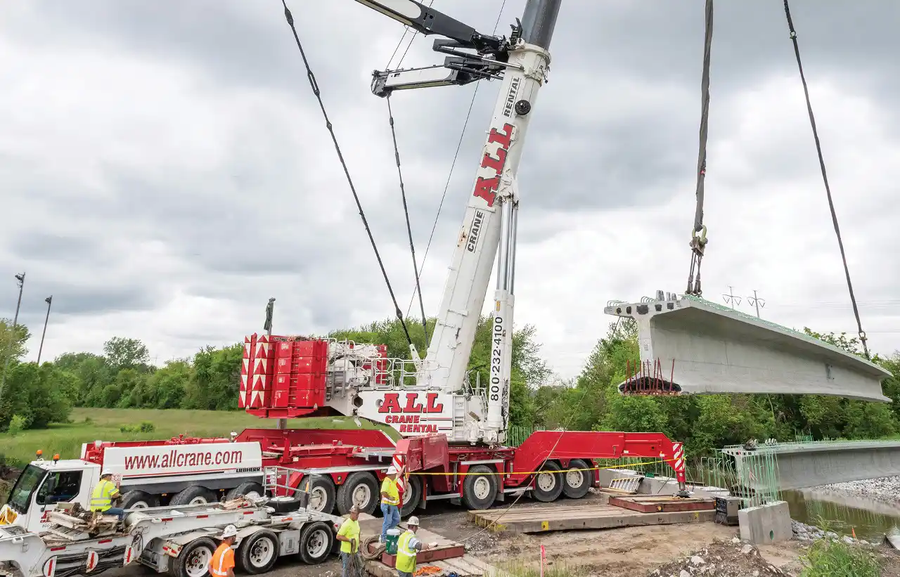 A crane rented from ALL lifting an I-beam.